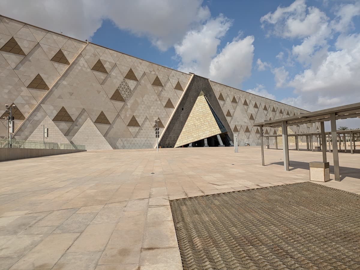 The distinctive triangular main facade of the Grand Egyptian Museum near Giza in morning light — pale limestone, clear sky.