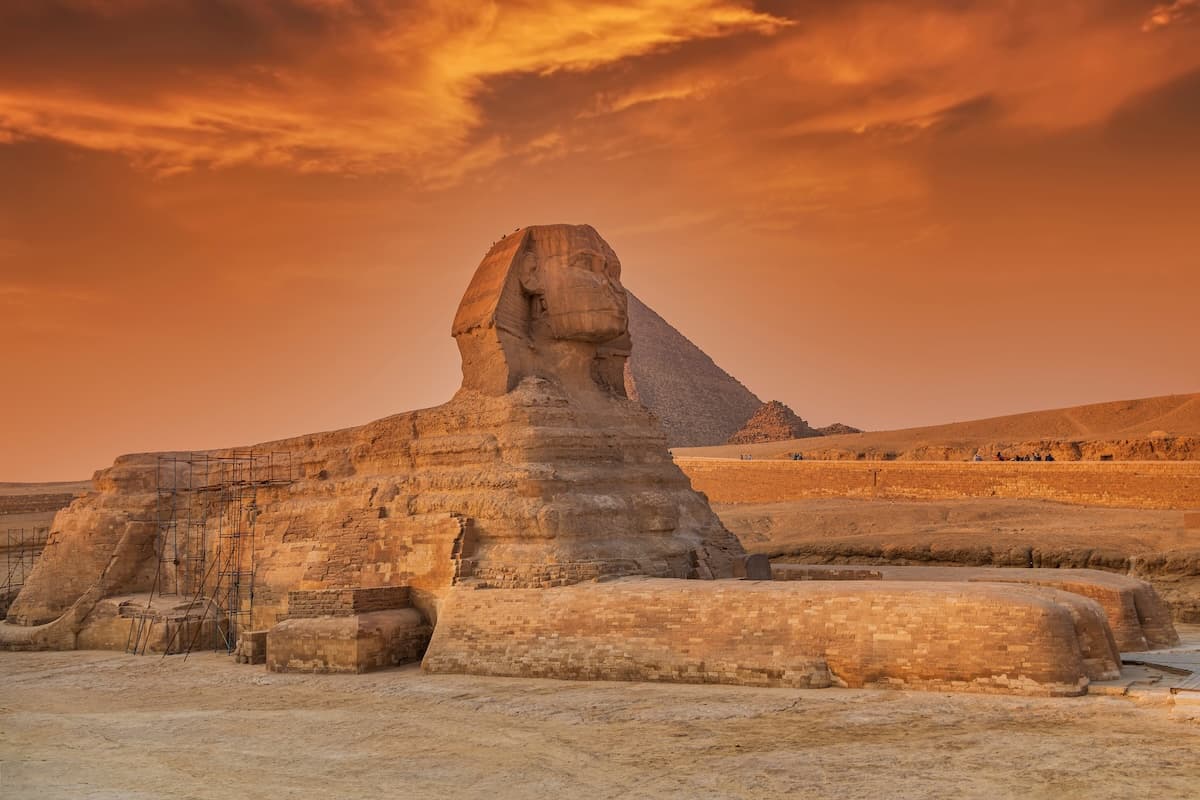 The Great Sphinx of Giza in front of the Pyramid of Khafre under an orange-and-pink sunset sky.