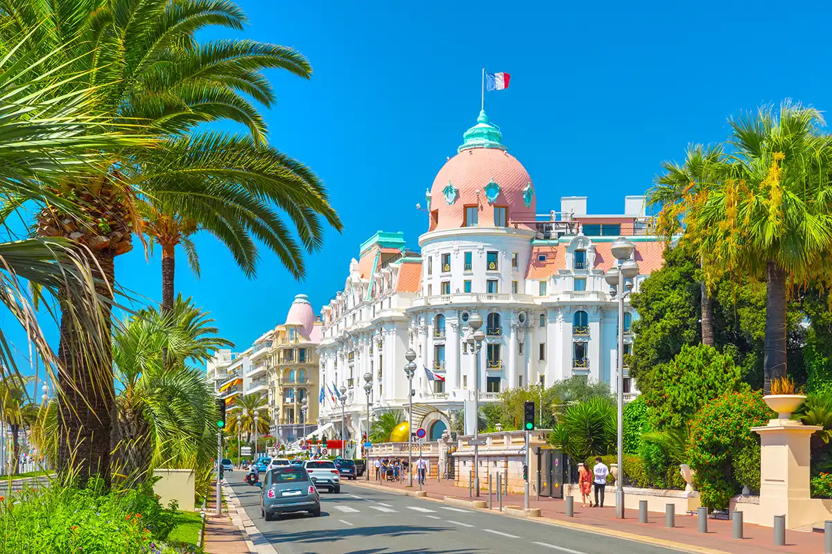 Die geschwungene Promenade des Anglais in Nizza am türkisfarbenen Mittelmeer, dahinter die Stadt.